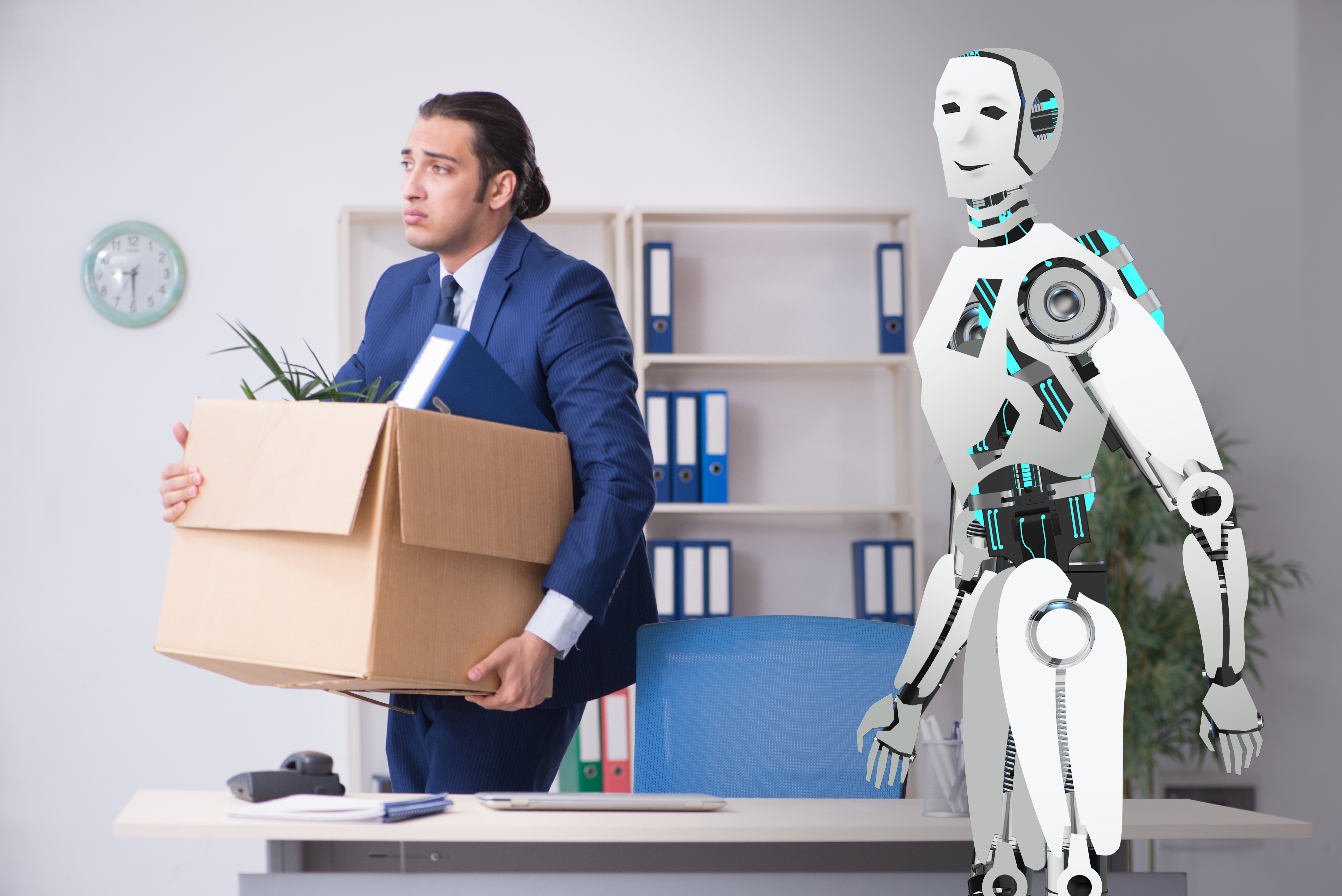 A man in a business suit is holding a box of filled with things you would find on a desk in a office. Behind the man is an Android robot .